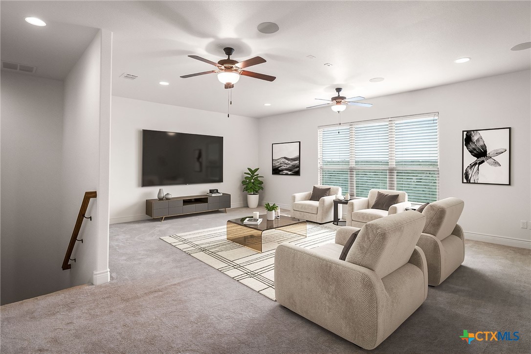 Furnished living room with cream seating, a wall-mounted TV, and large windows with blinds.