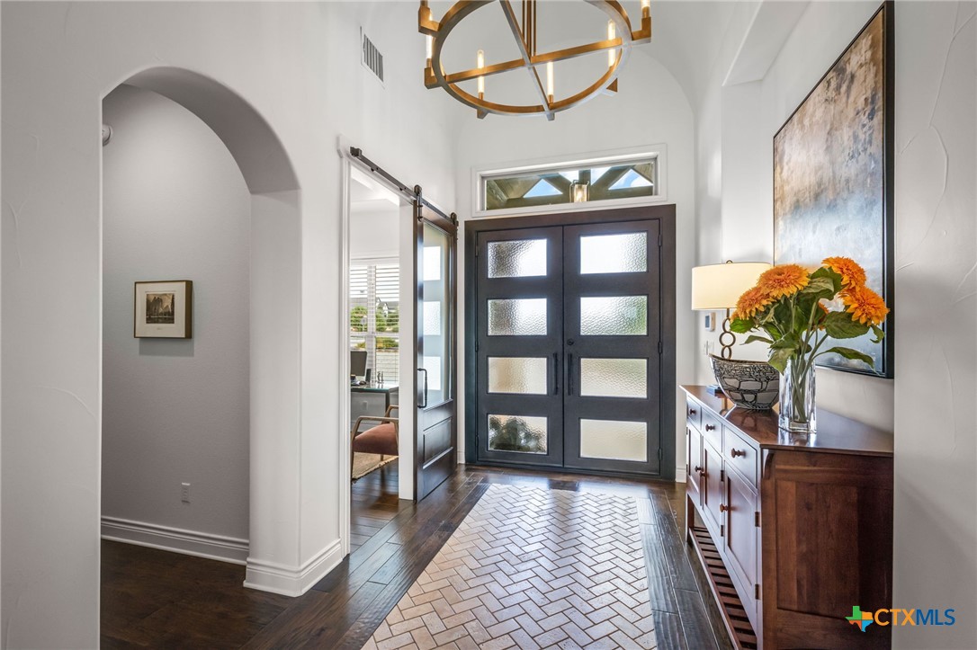 Foyer with a dark double front door, herringbone tile, and a wood console topped with orange flowers.
