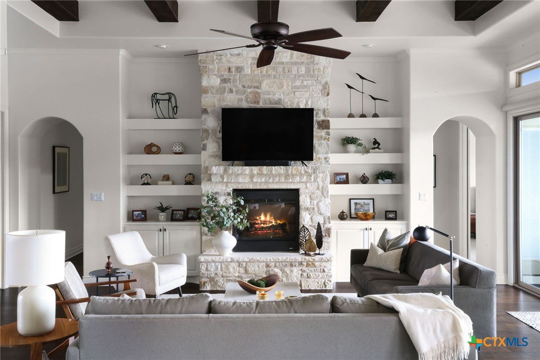 Living room with a stone fireplace, built-in shelves, exposed ceiling beams, and gray seating.