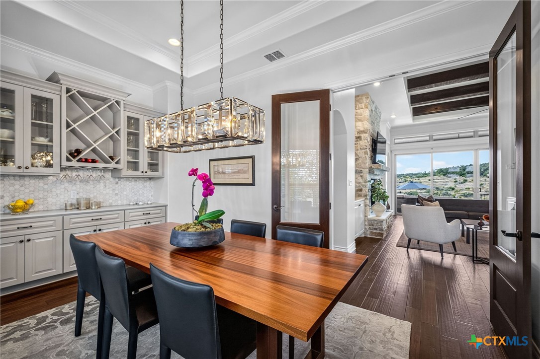 Dining room with a long wooden table, crystal chandelier, white cabinetry, and views of a rocky landscape.