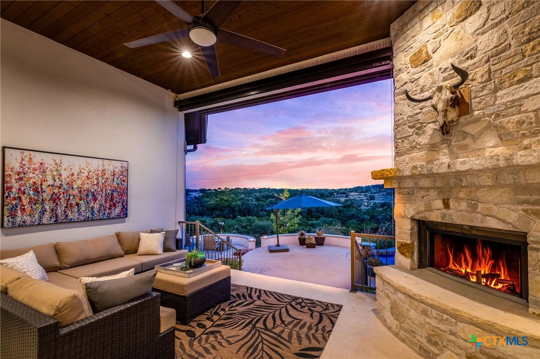 Living room with a stone fireplace and wide-open terrace view at dusk.