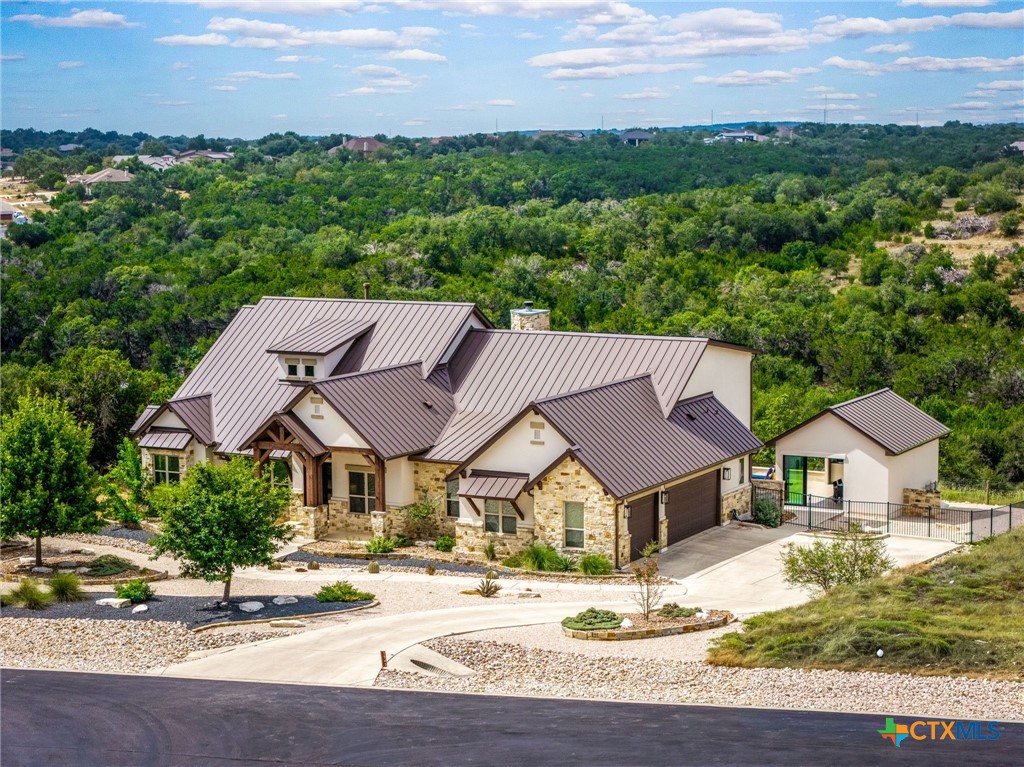 Aerial view of a stone home with metal roofs, a detached outbuilding, and surrounding woodland.