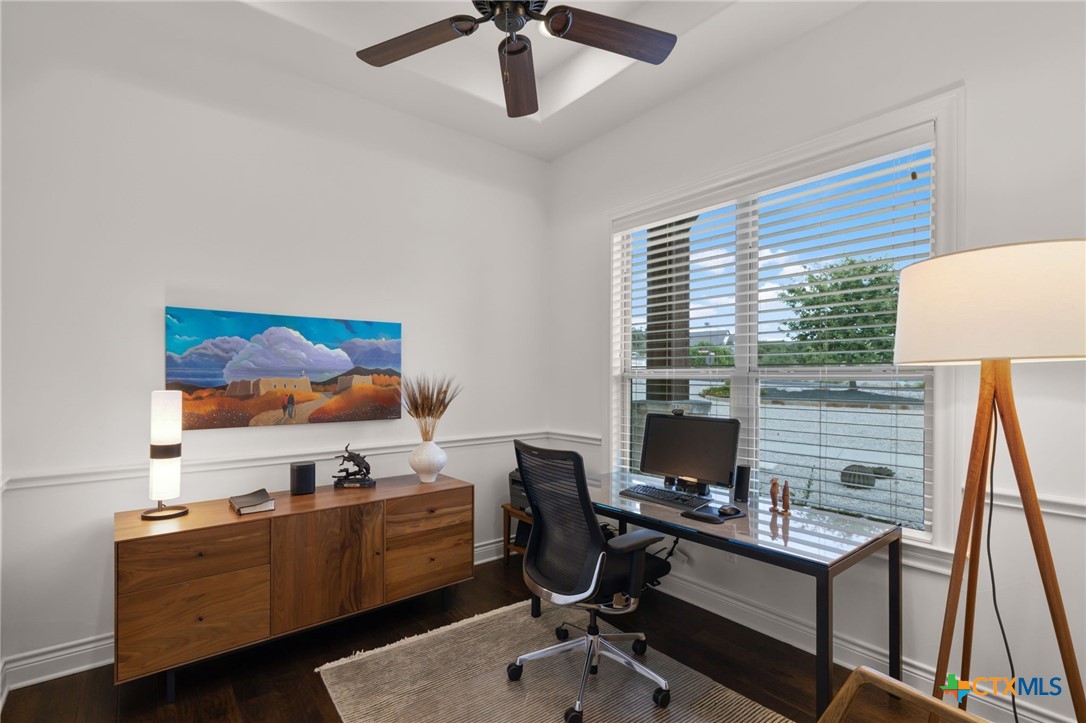 Furnished home office with a walnut credenza, desk by a large window, and colorful landscape artwork.