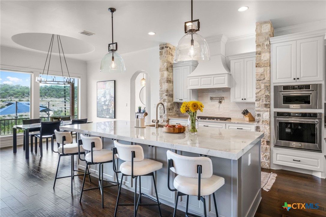 Open kitchen with a large white island, stone accents, and windows overlooking greenery.