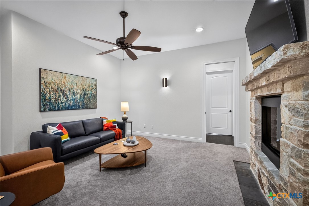 Living room with a stone fireplace, wall-mounted television, and dark sofa.