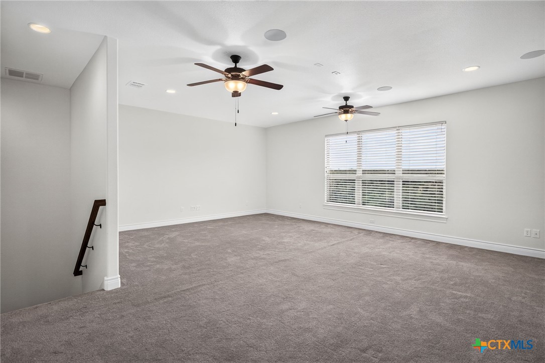 Empty carpeted room with two ceiling fans and a large window with blinds.