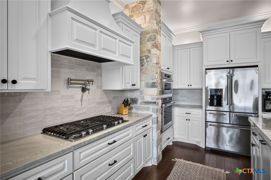 Kitchen with white cabinetry, gas cooktop, stainless appliances, and a stone column.