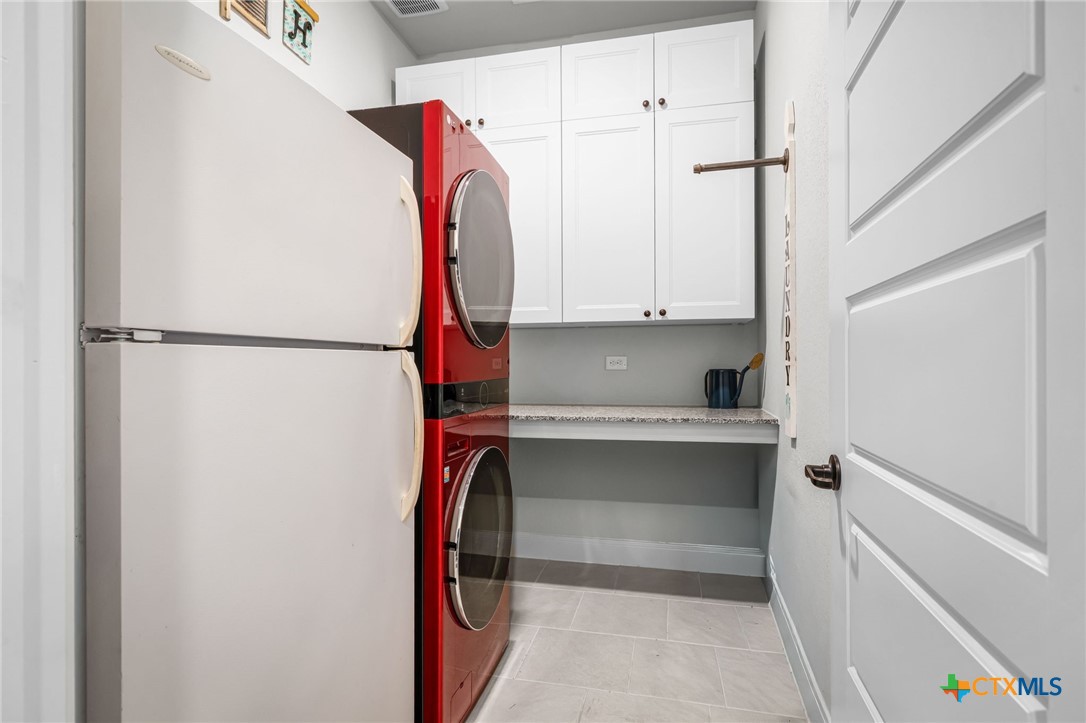 Laundry room with red stacked washer and dryer, white refrigerator, and upper cabinets.