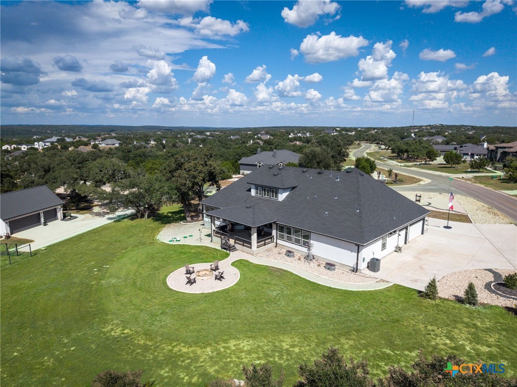 Aerial view of a home with a broad lawn, covered porch, and circular fire pit seating area.