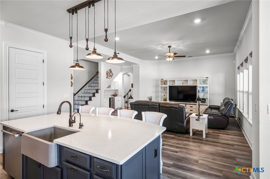 Open kitchen with a large island and farmhouse sink adjoining a furnished living room.