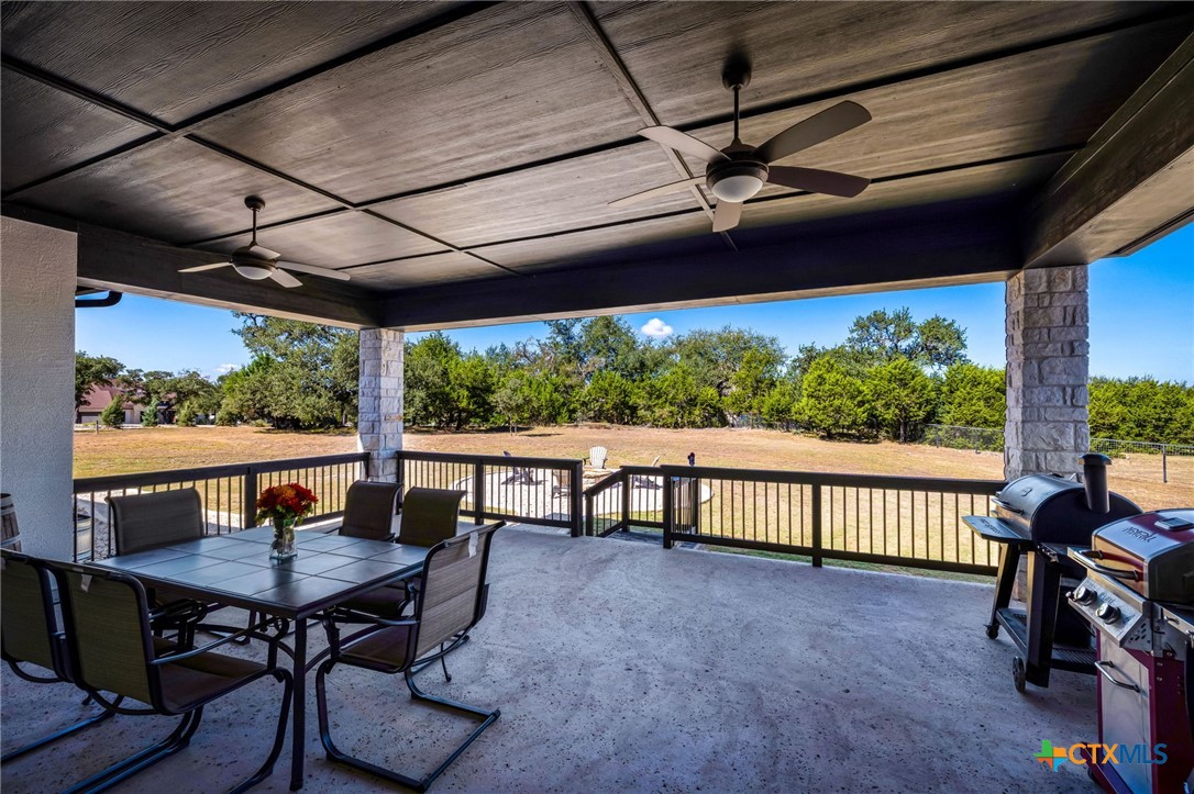 Covered patio with ceiling fans, dining set, and barbecue overlooking a fenced backyard.