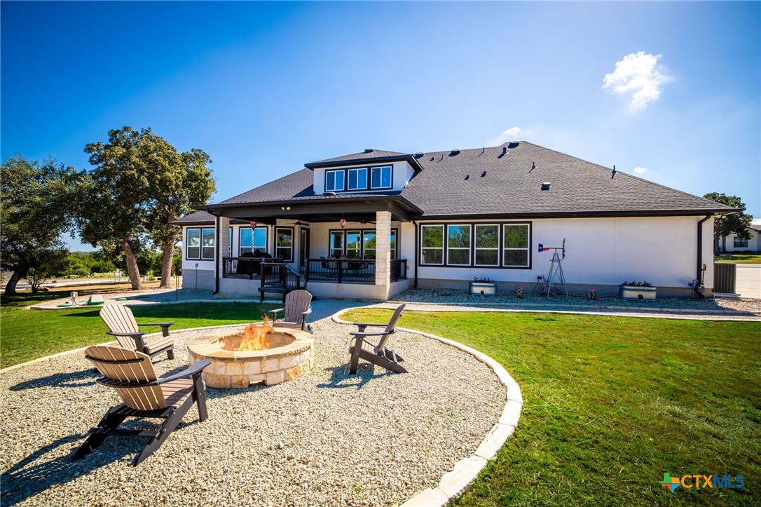 Rear of a single-story home with a covered patio and gravel fire-pit seating area.