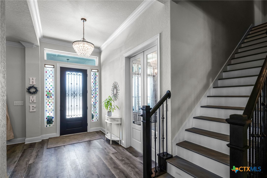 Entry foyer with stained-glass sidelights, a crystal chandelier, and a dark-railed staircase.