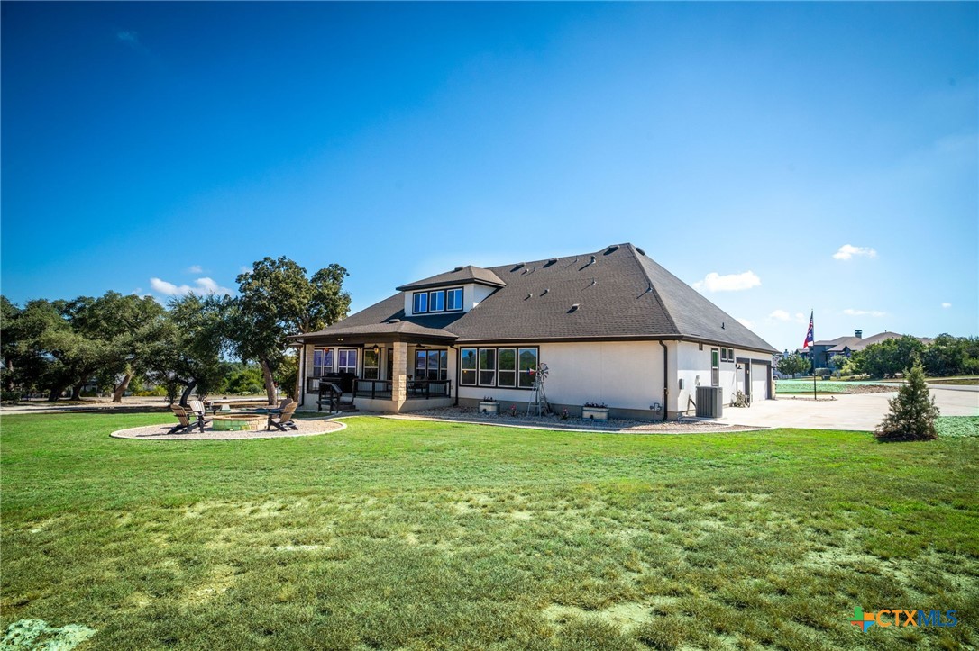 Home’s rear exterior with a covered patio and circular fire pit seating area across a broad lawn.
