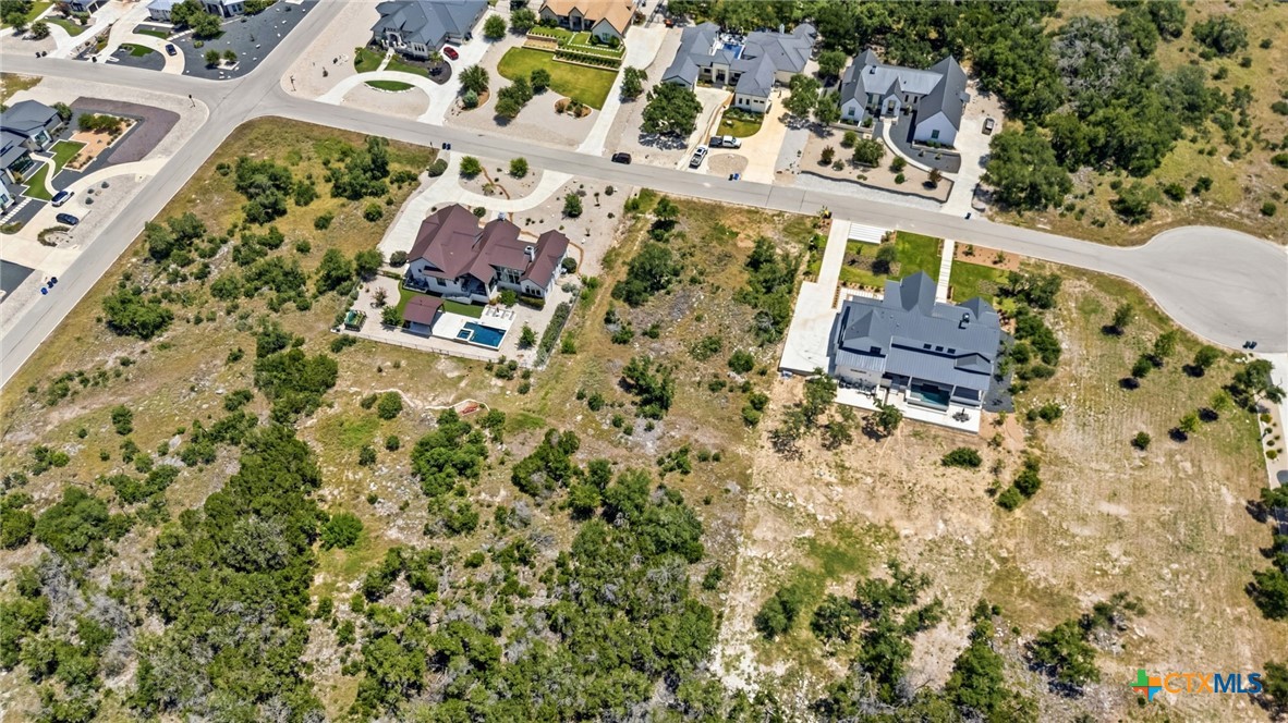 Aerial view of a brush-covered vacant lot beside homes and a residential street.