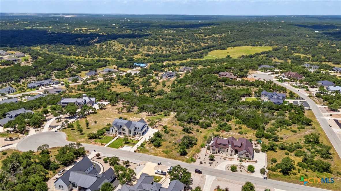Aerial view of homes and curving streets bordered by open lots and wooded countryside.