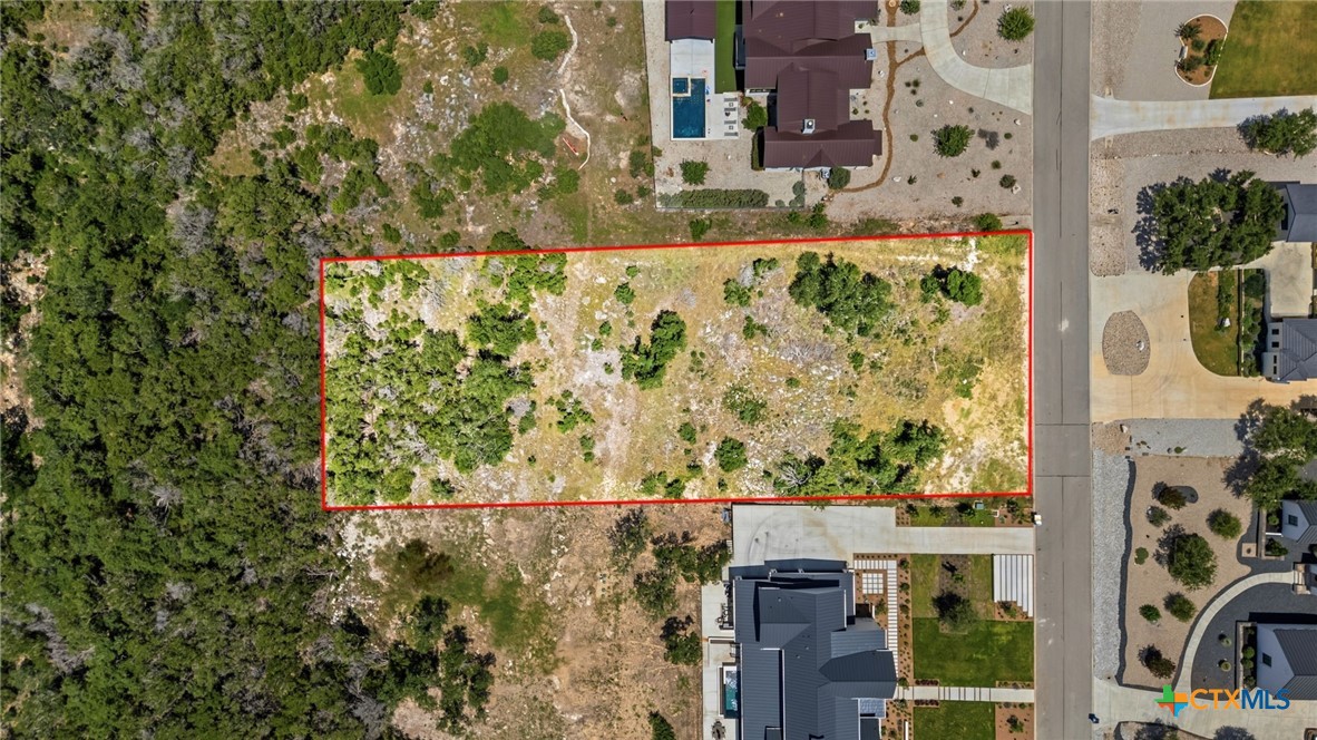 Vacant rocky lot outlined in red beside a residential street and neighboring homes.