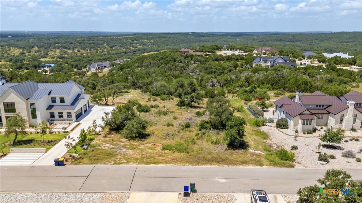 Aerial view of a vacant residential lot between homes, with wooded hills beyond.