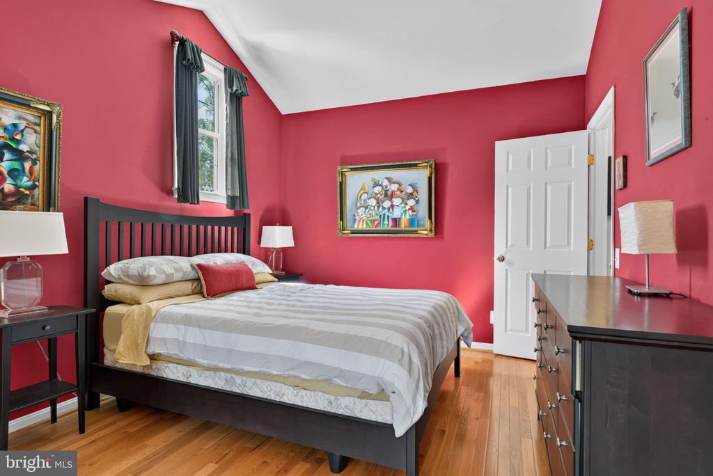 Bedroom with coral-red walls, a black bed, striped bedding, and hardwood floors.