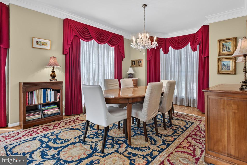 Dining room with an oval table, red drapes, chandelier, and ornate patterned rug.