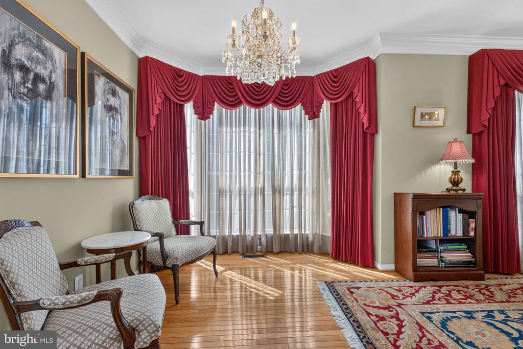 Living room with red drapes, a crystal chandelier, patterned chairs, and polished hardwood floors.