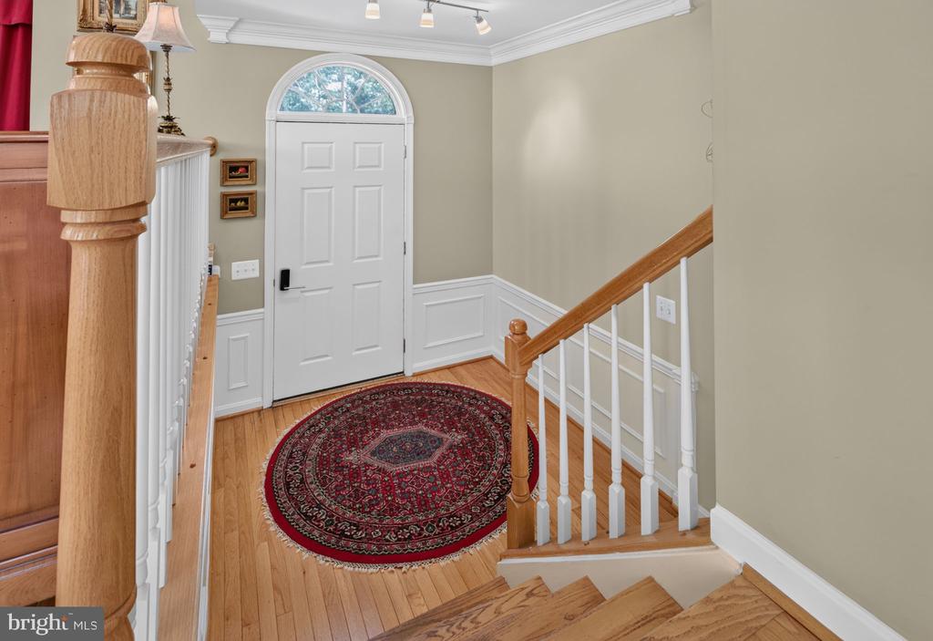 Entry foyer with an arched white front door, hardwood staircase, and round red patterned rug.