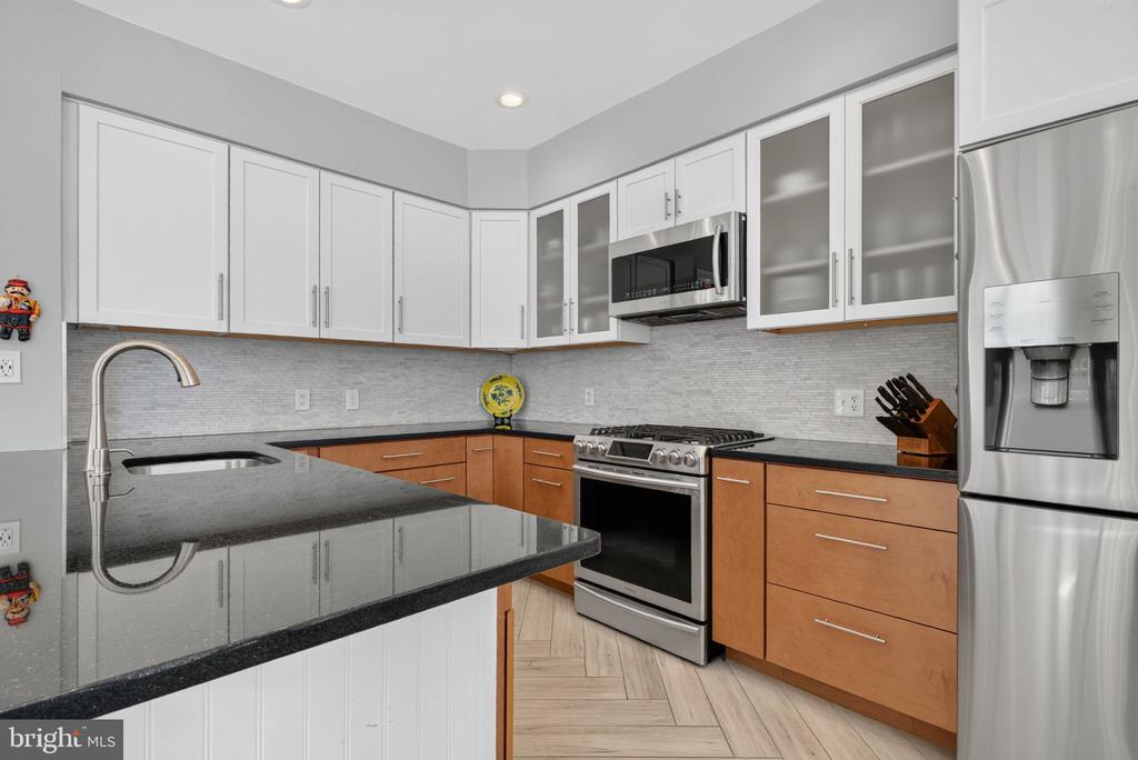 Kitchen with white and wood cabinetry, dark countertops, and stainless steel appliances.