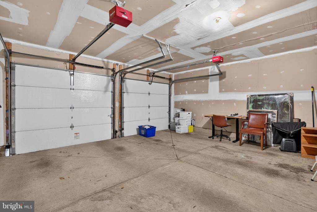 Spacious garage with two overhead doors, unfinished drywall, and a concrete floor.