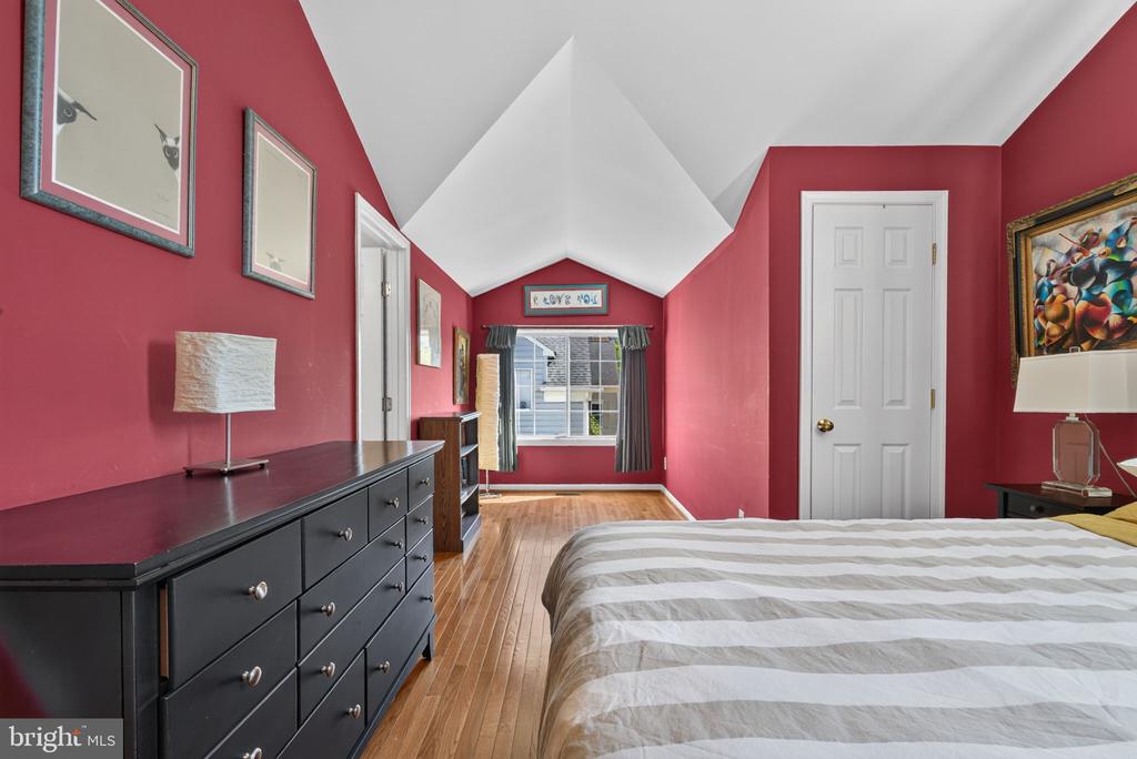 Bedroom with red walls, a vaulted ceiling, hardwood floors, and a large window.