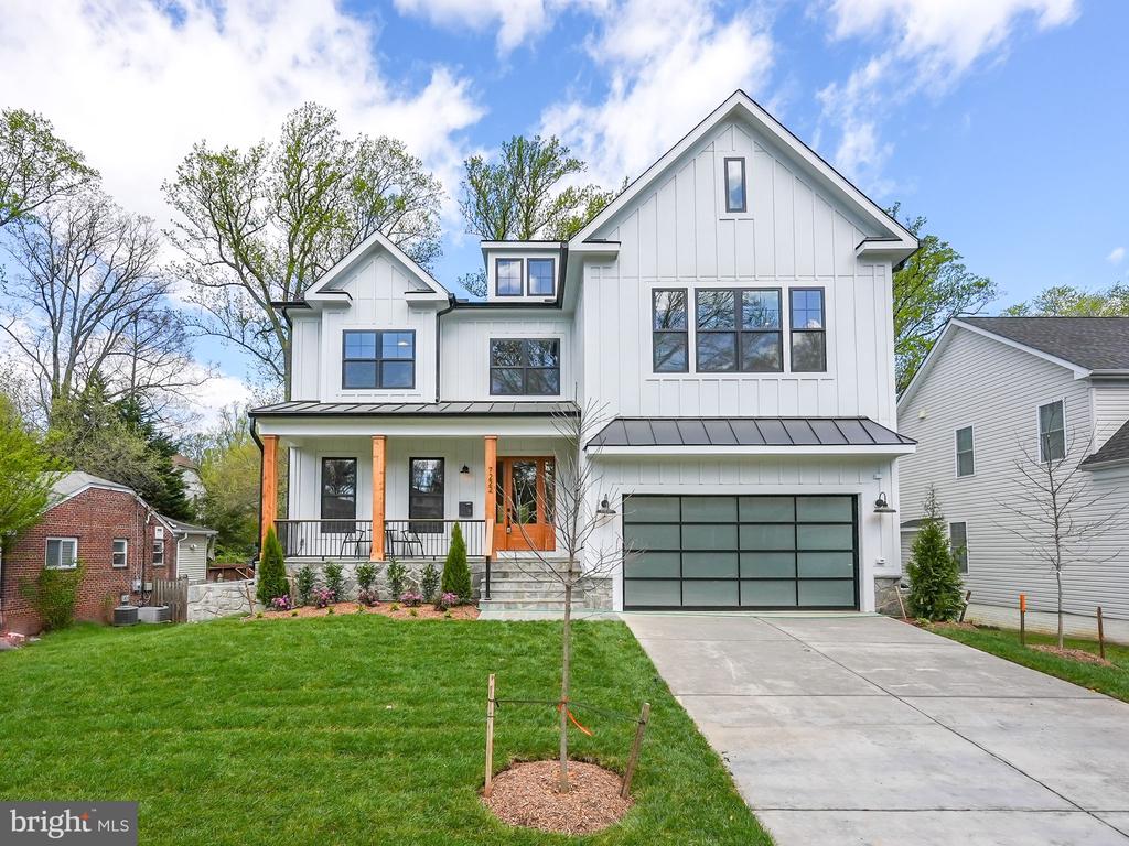 White two-story farmhouse with a covered porch, dark-framed windows, and a wide driveway.