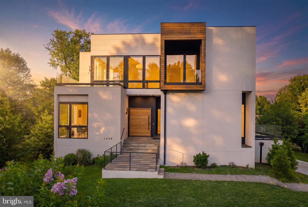 Modern white home with wood accents, broad windows, and landscaped entry at sunset.