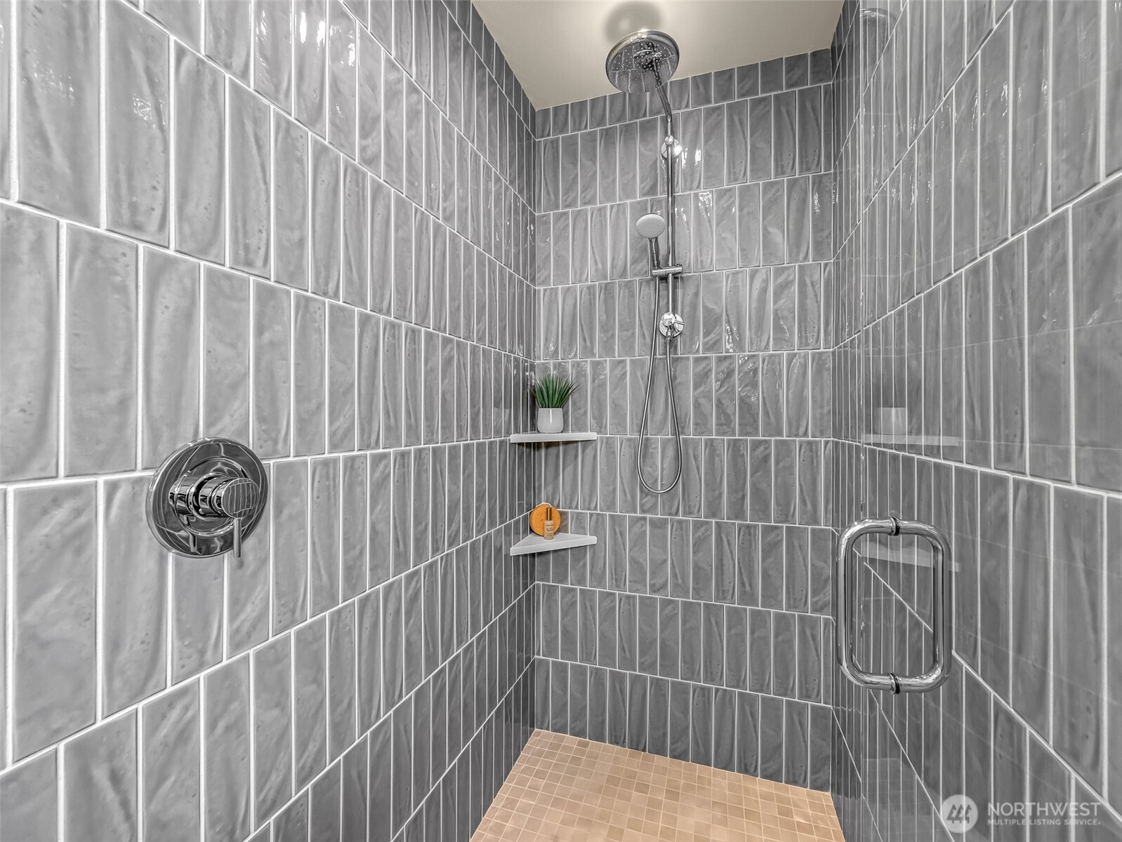 Walk-in shower with gray tile walls, rainfall showerhead, handheld sprayer, and glass door.