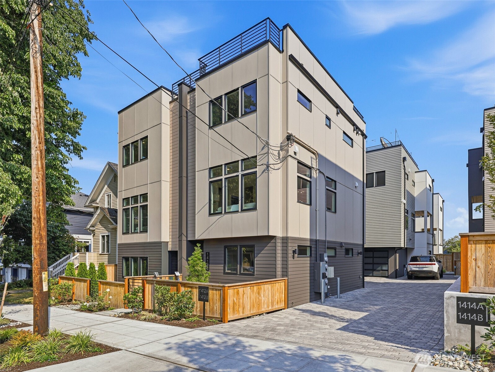 Modern multi-story townhouse with a rooftop deck, large windows, and a fenced front garden.