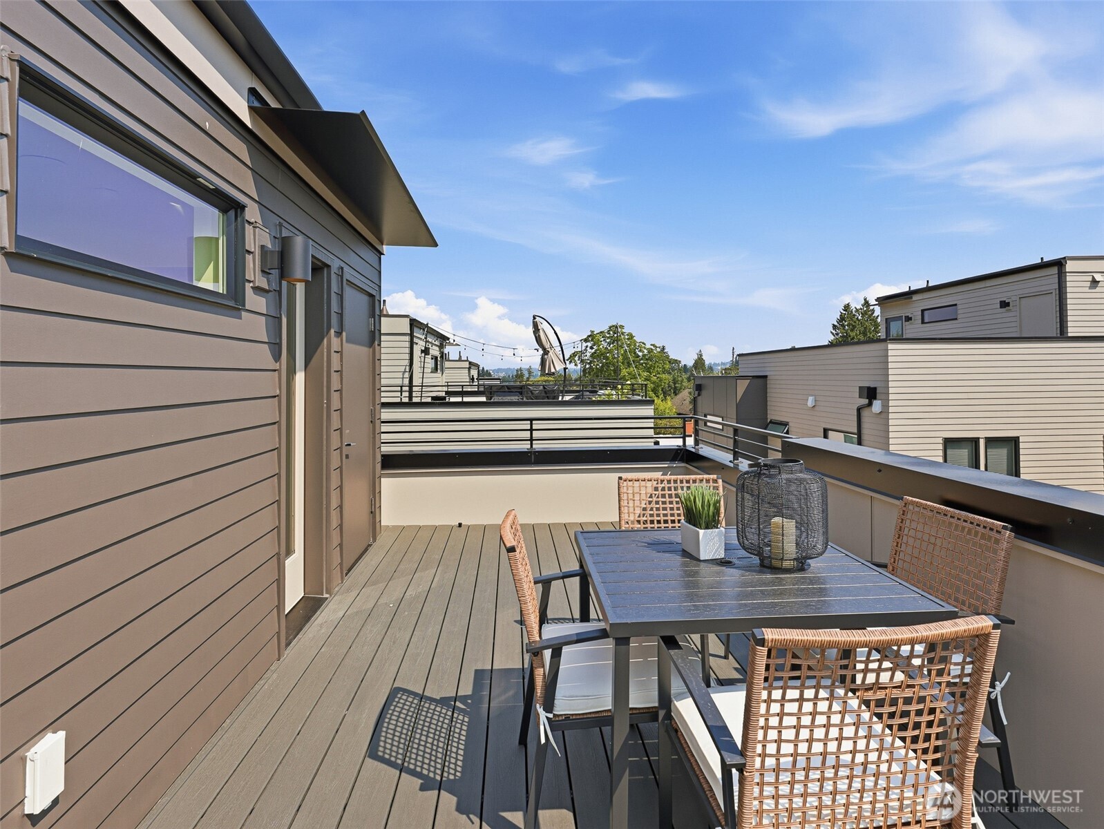 Rooftop deck with a dining table and woven chairs beside a modern home.