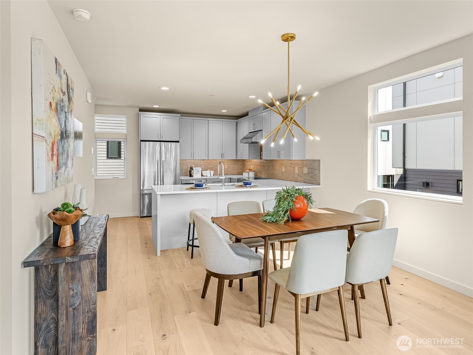 Dining area with a wood table and gold chandelier beside a modern kitchen with gray cabinets.