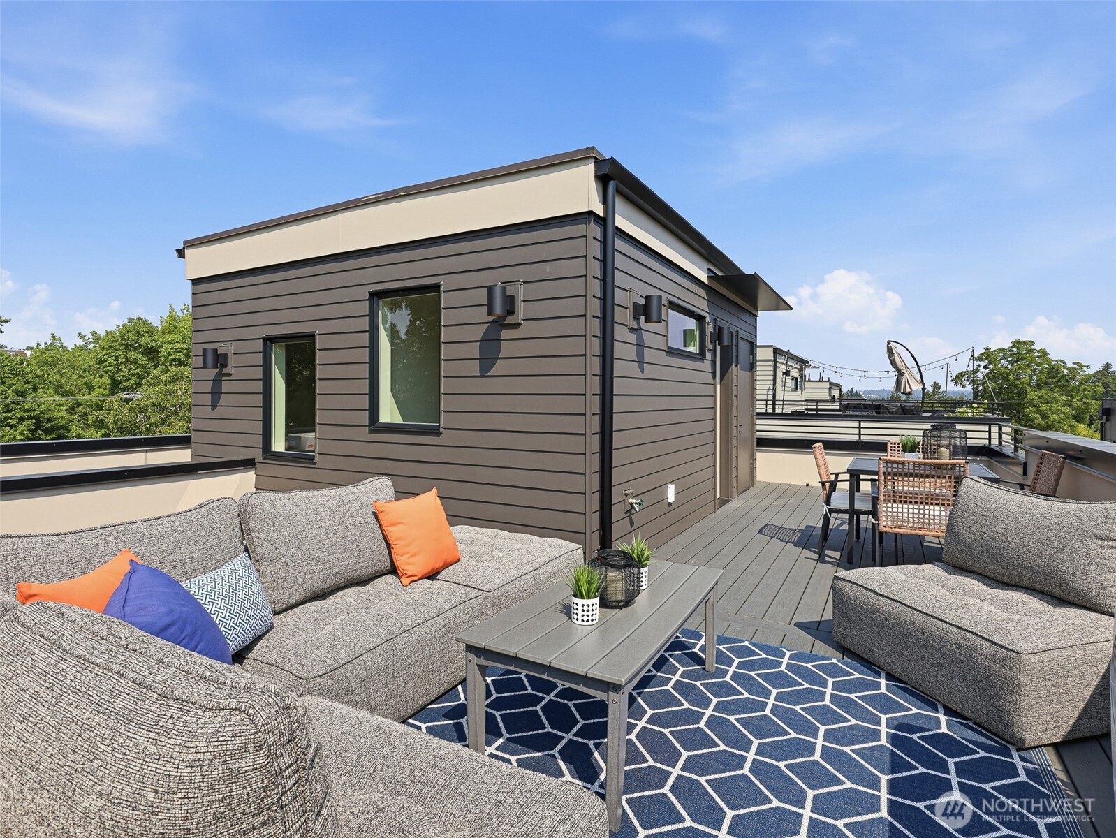 Rooftop deck with gray sofas, a blue geometric rug, and an outdoor dining set.