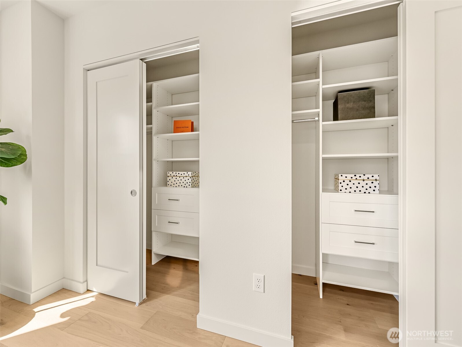 Walk-in closet with two white built-in shelving units, drawers, and light wood flooring.