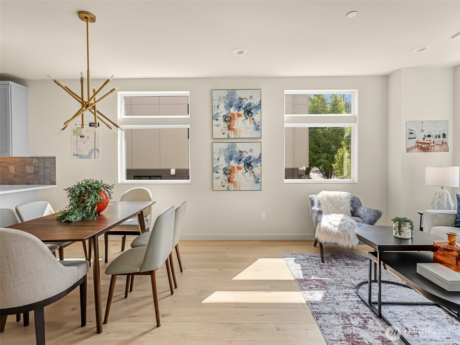 Furnished living and dining room with light wood floors, large windows, and a brass chandelier.