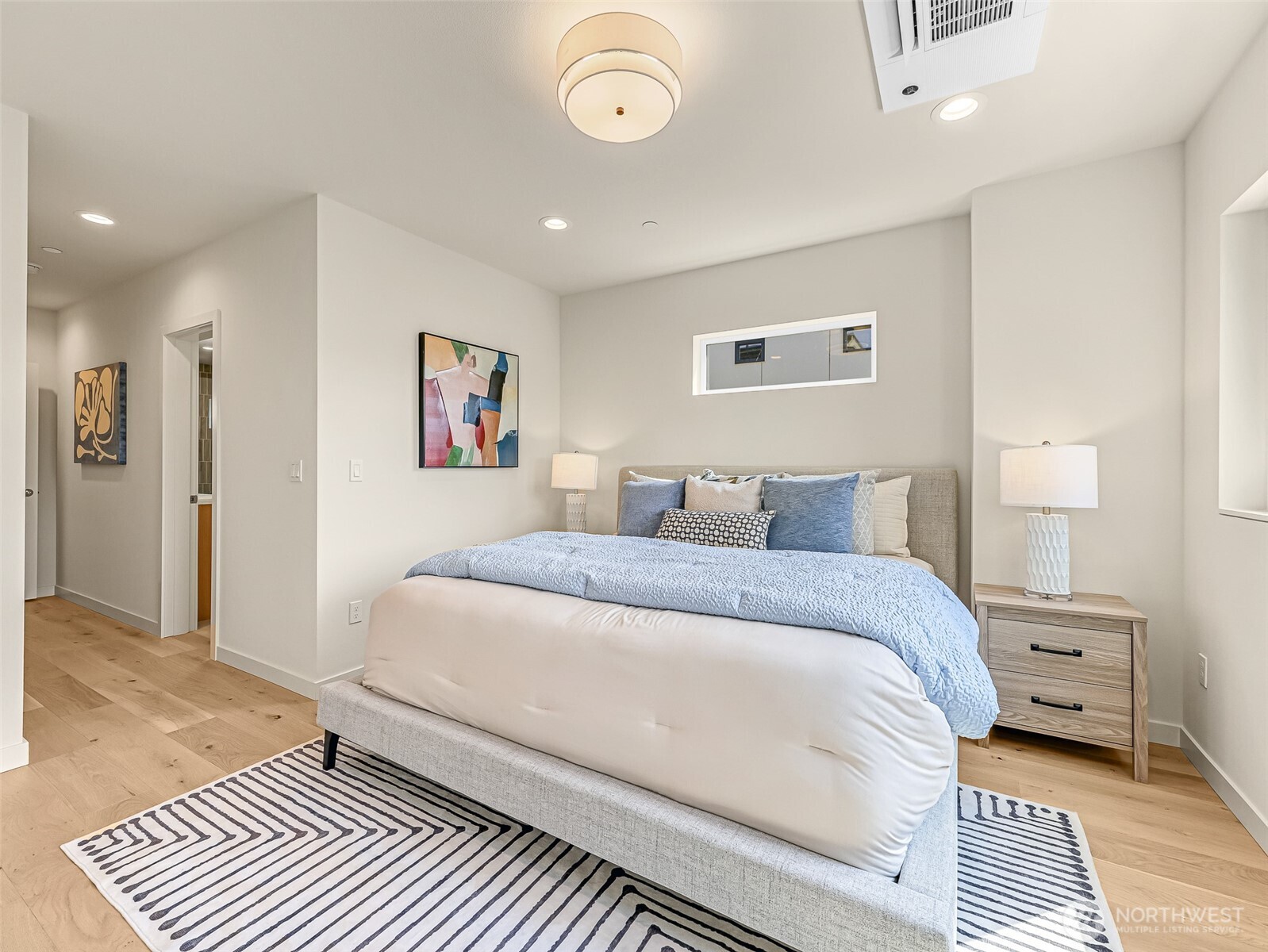 Staged bedroom with a large bed, pale blue bedding, matching nightstands, and a striped rug.