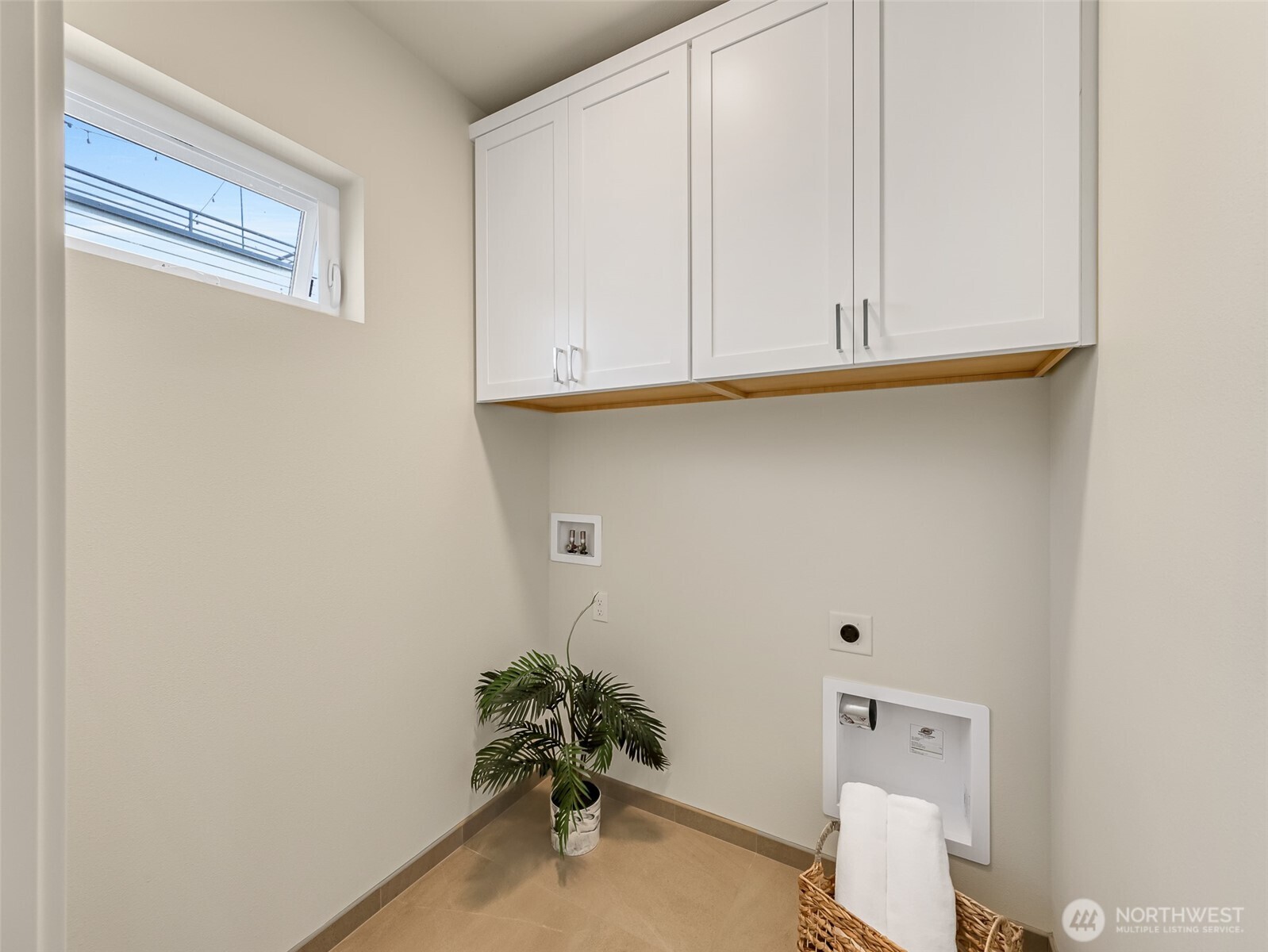 Laundry area with white overhead cabinets, washer hookups, and a high horizontal window.