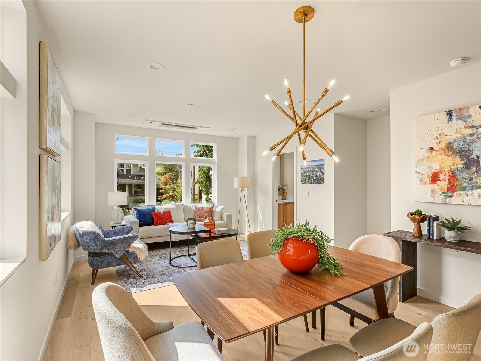 Open-plan living and dining room with a wood table, large windows, and a sculptural gold chandelier.