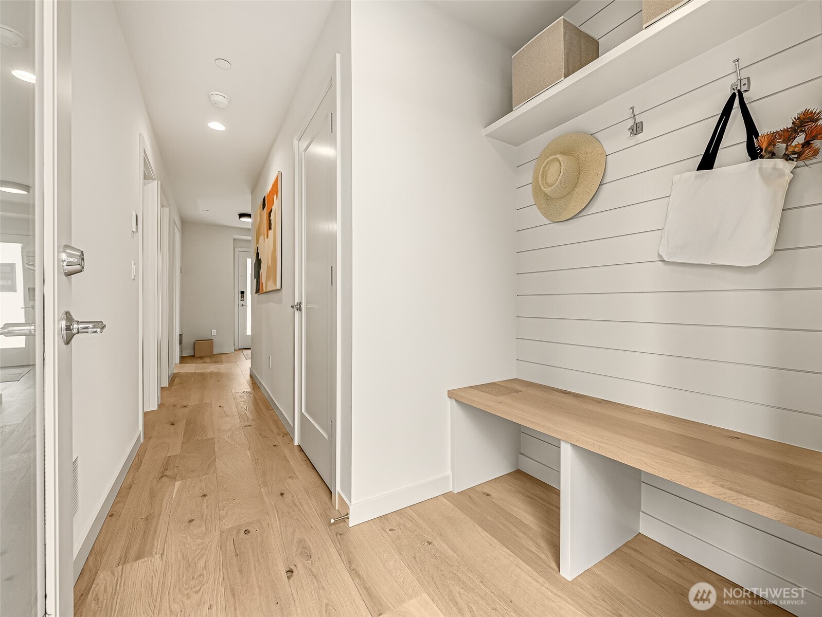 Entry hall with a built-in wood bench, shiplap wall, hooks, and light oak flooring.