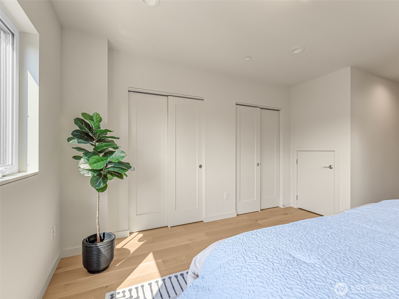 Bright bedroom with white closet doors, a potted plant, and pale blue bedding.