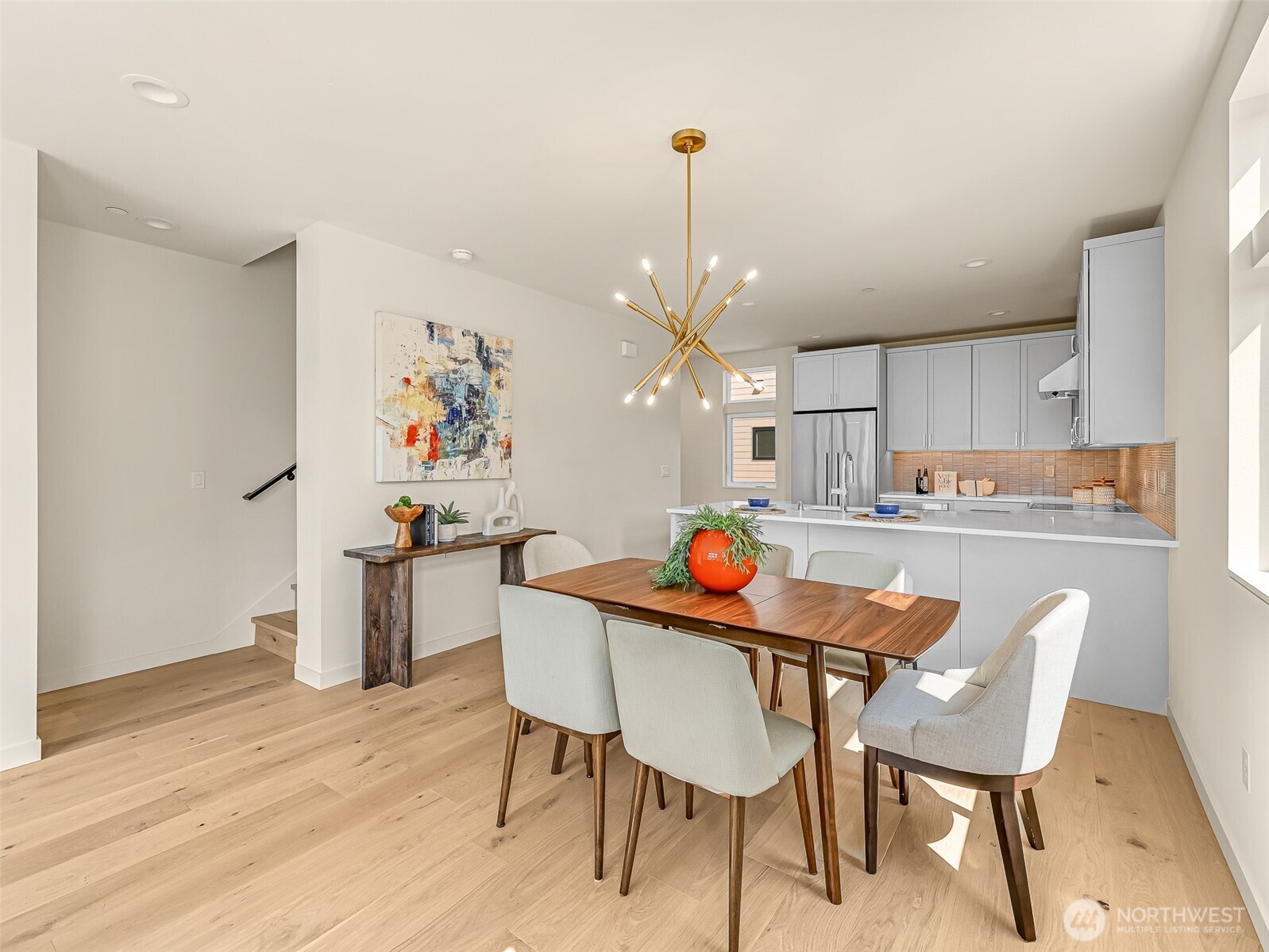 Dining area with a wood table and upholstered chairs beside a bright modern kitchen.