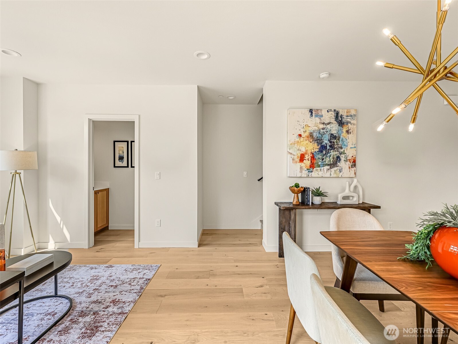 Open-plan living and dining area with light oak floors and a gold starburst chandelier.