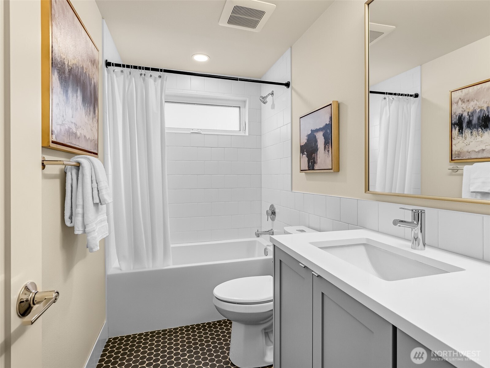 Bathroom with a gray vanity, white tiled tub and shower, and patterned black-and-white floor tile.