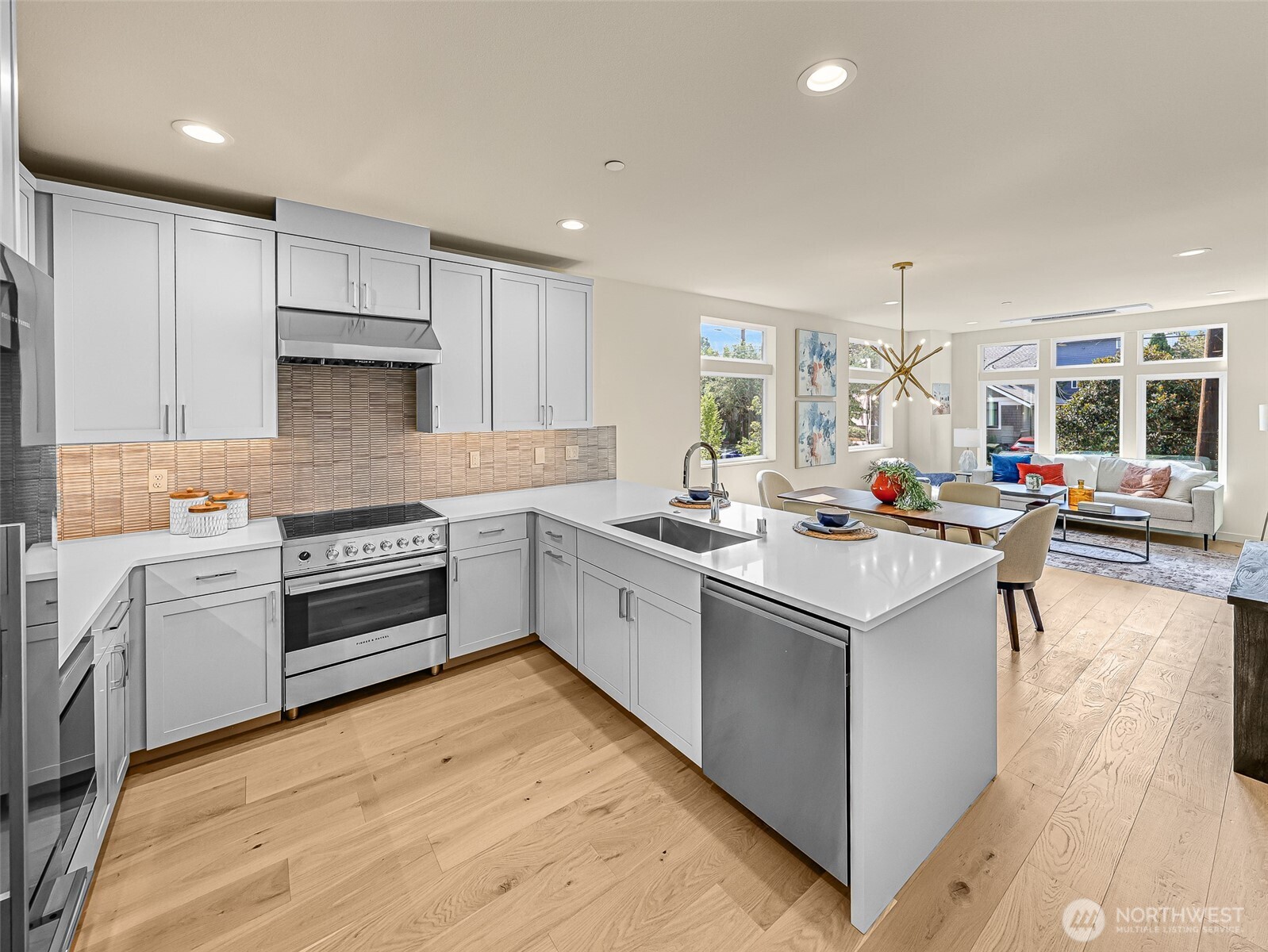 Staged kitchen with a large white island, stainless steel range, and open dining and living area.