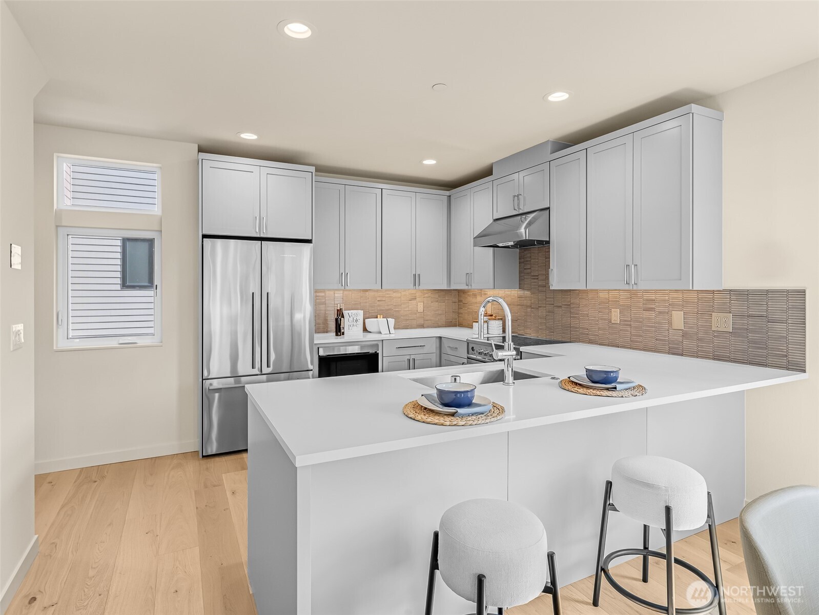 Modern kitchen with a large white island, gray cabinets, stainless steel appliances, and metallic tile backsplash.