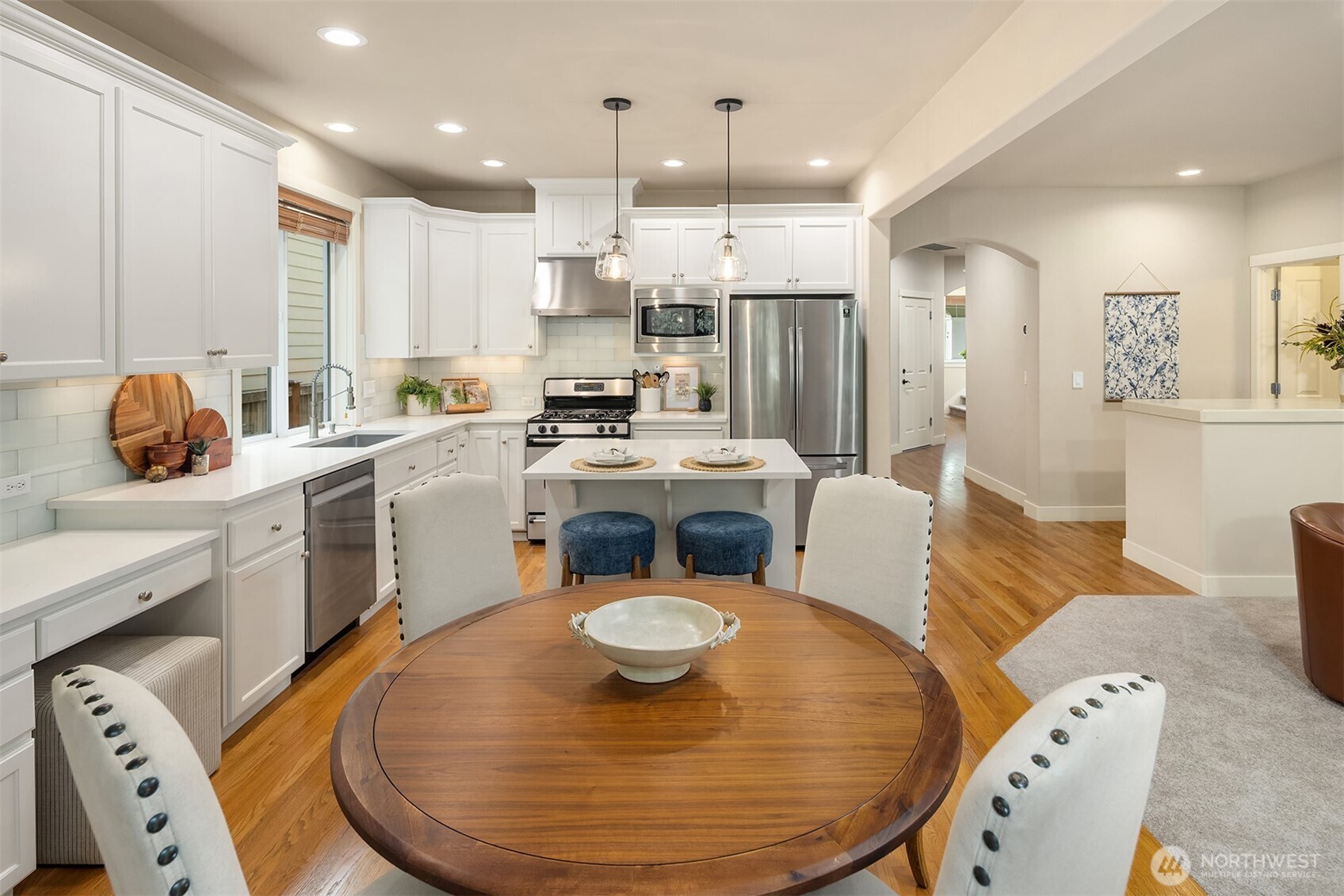Kitchen with white shaker cabinets, stainless steel appliances, a white island, and a round wooden dining table.
