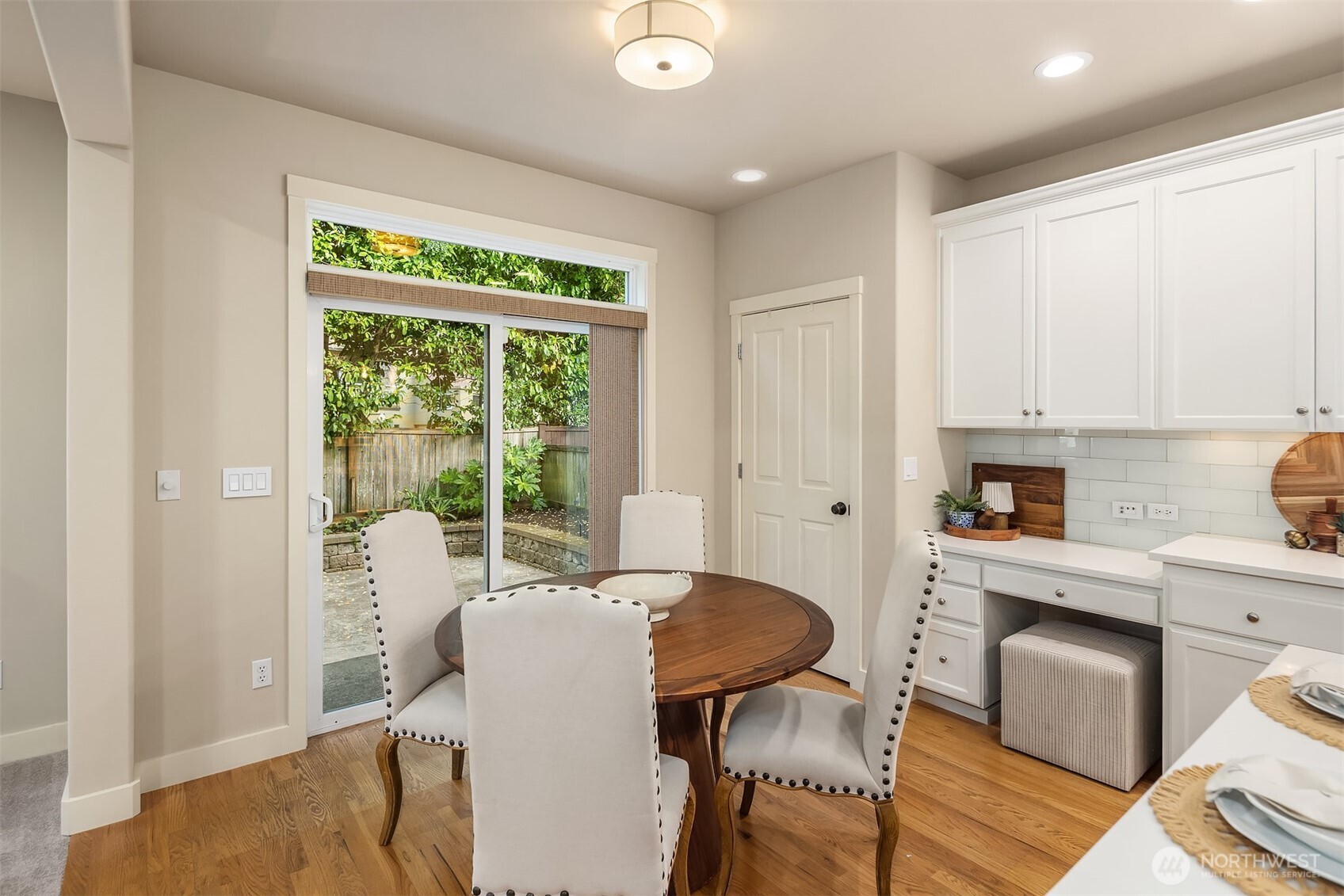 Kitchen dining nook with white cabinets, round wood table, and sliding glass door to a garden.
